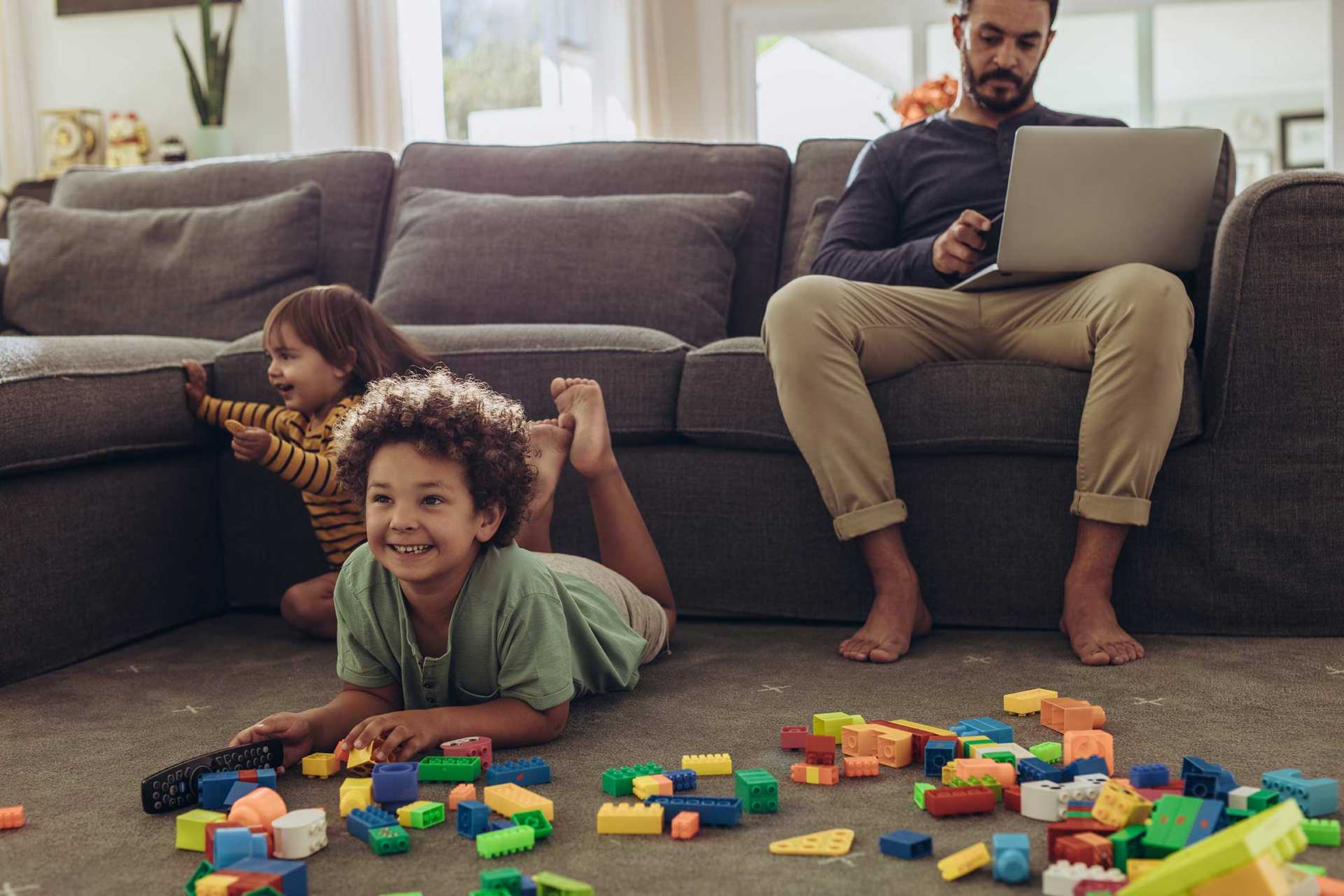 Dad working on the couch with laptop in the living room while kids play